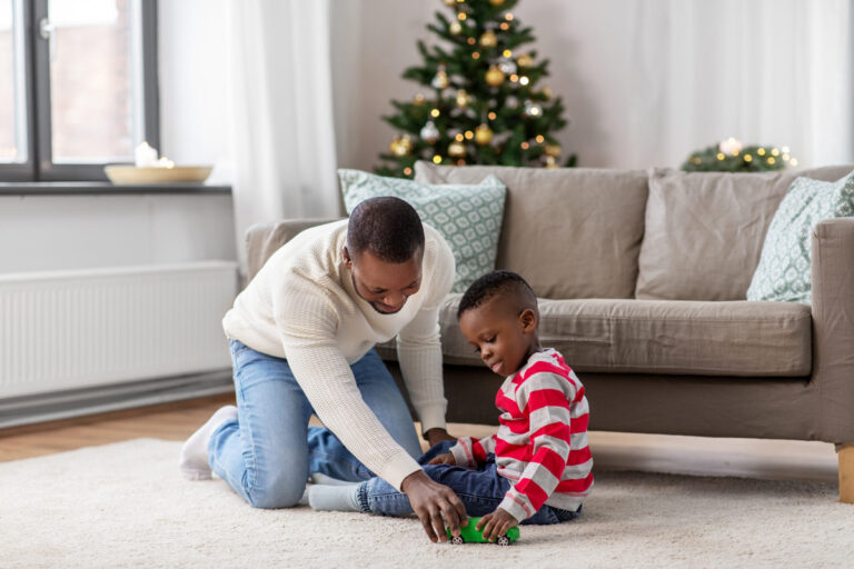 Father and child sitting on floor by Christmas tree, playing together