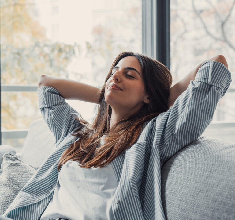 Woman relaxing in chair by window, stretching arms behind head